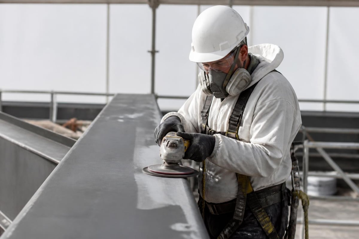 Worker in a safety harness grinding steel as surface preparation before painting